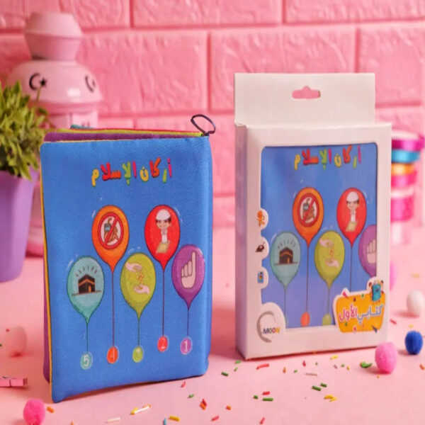 "كتاب قماش أزرق للأطفال بعنوان أركان الإسلام بجانب علبة التغليف الخاصة به، يُظهر رسومات تعليمية ملونة للأركان الخمسة، إصدار دار موون."