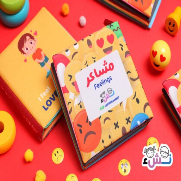"كتاب قماشي للأطفال بعنوان مشاعر Feelings من إصدار نشء، يظهر رموزاً تعبيرية ملونة على خلفية حمراء مبهجة مع ألعاب أطفال."