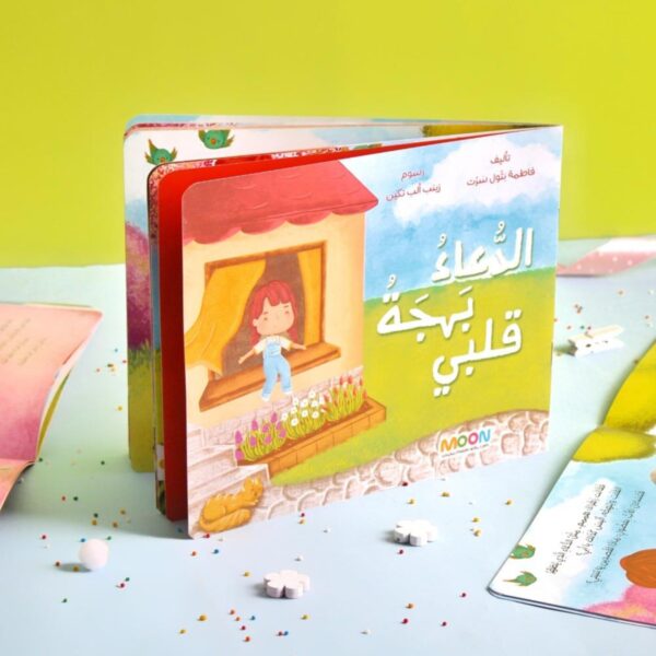 غلاف قصة الأطفال "الدعاء بهجة قلبي" من إصدارات MOON، يظهر طفلة تطل من نافذة منزلها وسط طبيعة خضراء، قصة تربوية لتعليم الأطفال قيمة الدعاء.
